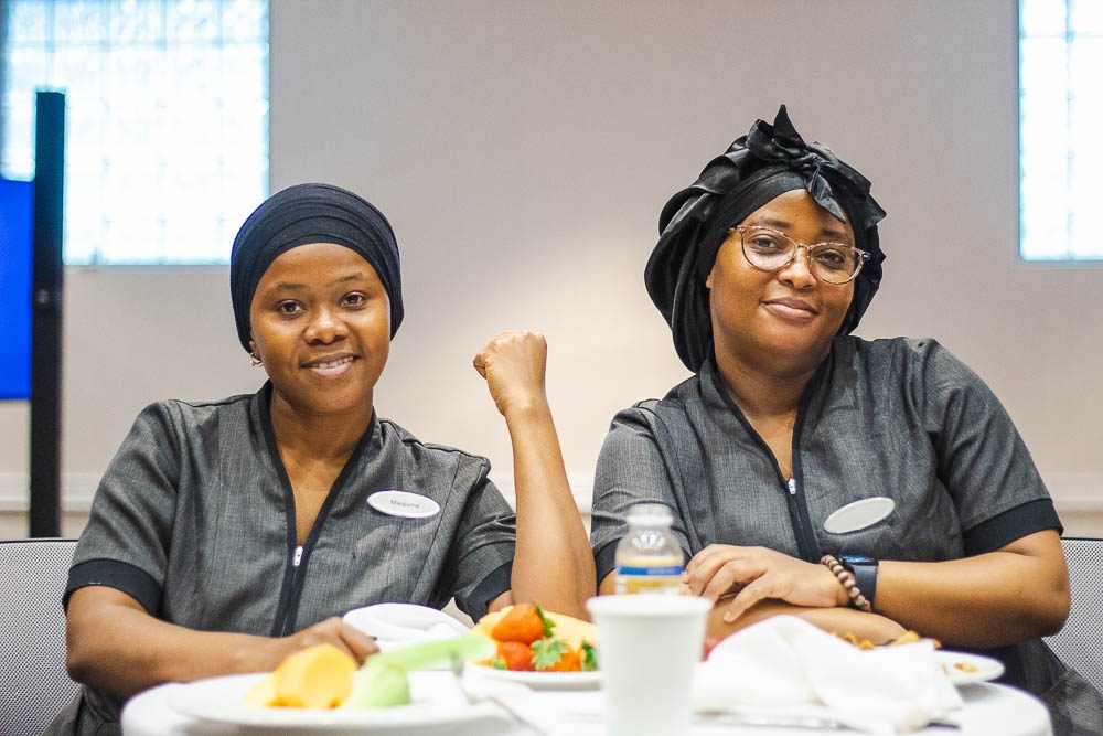 Two smiling team members in grey uniforms at a lunch table