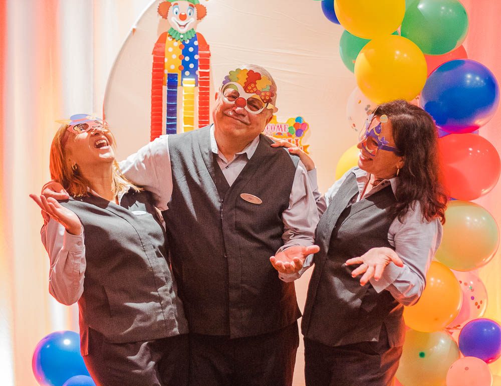 Three team members laughing in party masks at a balloon photo booth